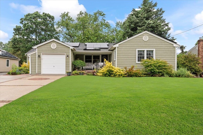 Ranch-style house featuring solar panels, a front lawn, driveway, and a garage