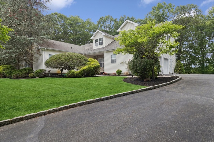 View of property hidden behind natural elements featuring a front yard, asphalt driveway, and a shingled roof