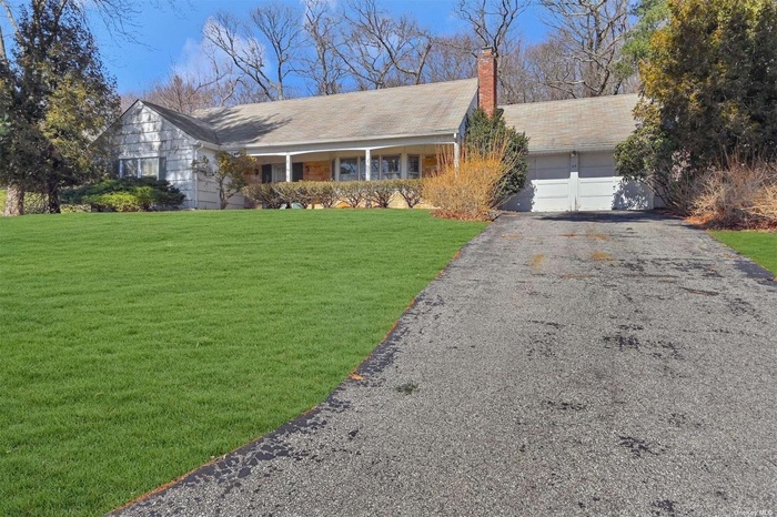 Ranch-style house with a chimney, an attached garage, a front lawn, and driveway