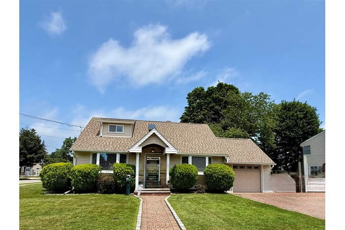 View of front facade with a front lawn, a shingled roof, decorative driveway, and a garage