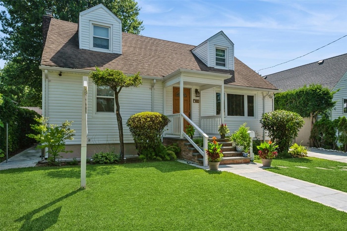 Cape cod-style house featuring roof with shingles, a front yard, and a chimney