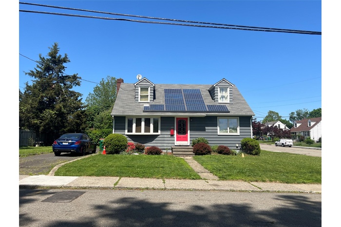 New england style home featuring roof mounted solar panels, a front lawn, entry steps, and a chimney