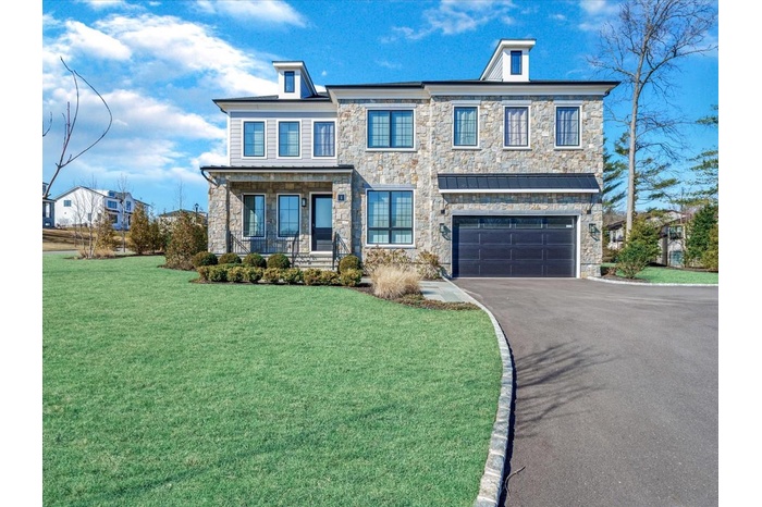 View of front of house featuring an attached garage, stone siding, aphalt driveway, a front yard, and a porch