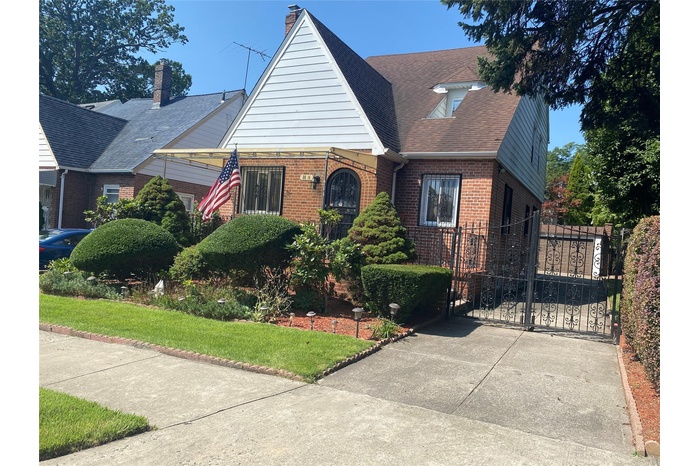 View of front facade with a gate, brick siding, and roof with shingles