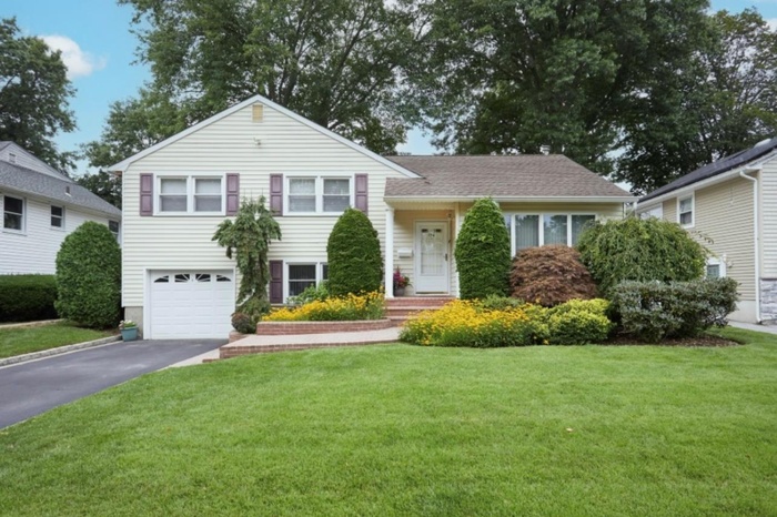 Split level home featuring an attached garage, driveway, a front lawn, and roof with shingles