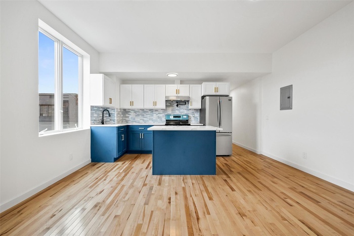 Kitchen featuring blue cabinetry, light countertops, light wood-type flooring, appliances with stainless steel finishes, and a kitchen island