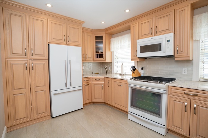 Kitchen featuring white appliances, light stone counters, recessed lighting, decorative backsplash, and glass insert cabinets