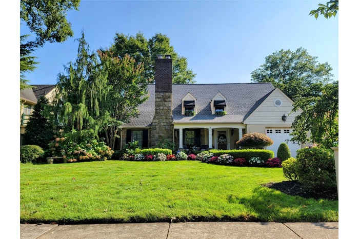 Expansive home with an attached garage, a front lawn, decorative driveway, covered porch, and roof with shingles