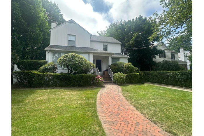 View of front of home with a chimney, a front yard, and a shingled roof