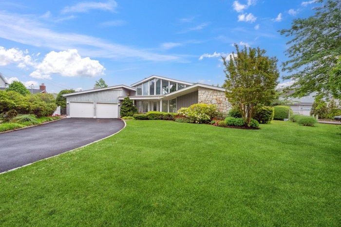 Mid-century modern home with asphalt driveway, stone siding, a front lawn, and a garage