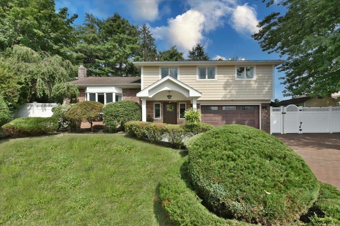 View of front facade featuring a gate, brick siding, an attached garage, a chimney, and driveway