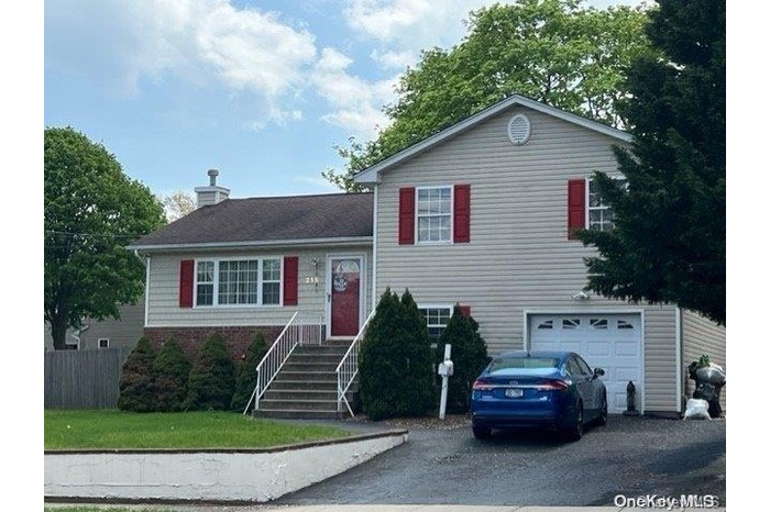 Split level home featuring an attached 1 car garage, asphalt driveway, a vinyl and brick siding