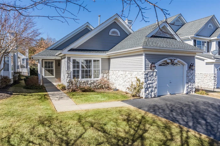 View of front of property with an attached garage, stone siding, aphalt driveway, and a front lawn
