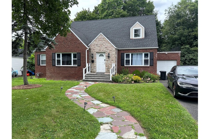 View of front facade featuring an attached garage, a front yard, and brick siding