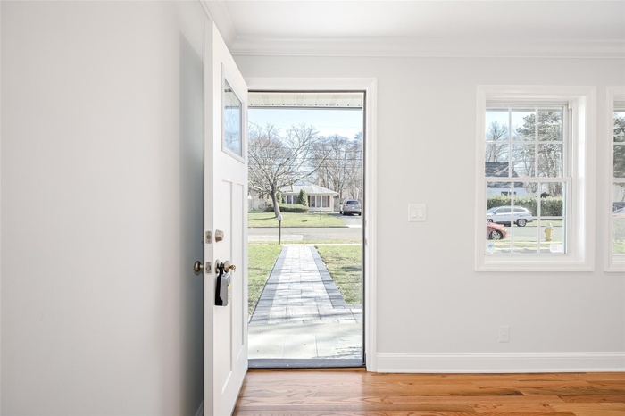 Doorway with ornamental molding, wood finished floors, and healthy amount of natural light