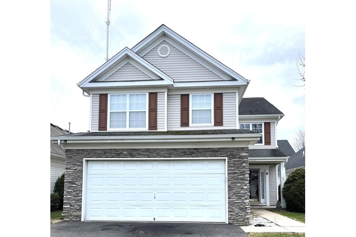 View of front facade with an attached garage, stone siding, and driveway