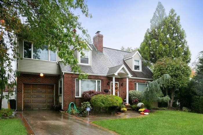 Cape cod-style house with brick siding, a garage, driveway, and a front yard