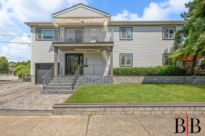 View of front of property featuring a balcony, a front lawn, an attached garage, and driveway