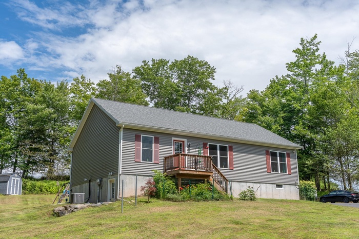 View of front of home with a wooden deck, a front lawn, stairs, and a storage shed