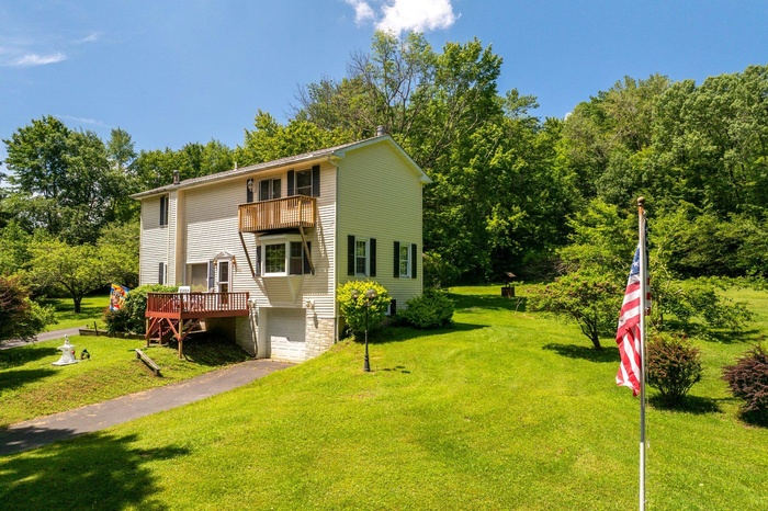View of front of property with a balcony, an attached garage, a front yard, and asphalt driveway
