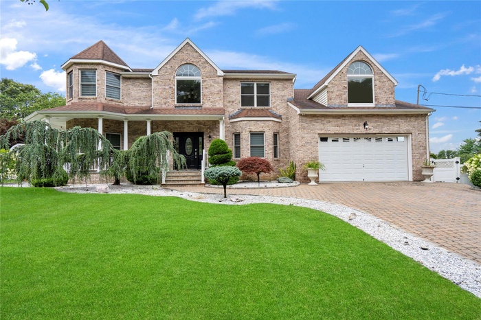 Traditional-style home with a front lawn, decorative driveway, brick siding, and covered porch