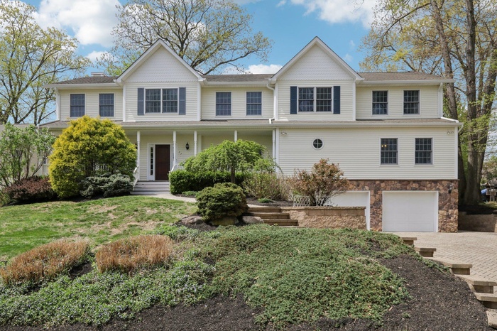 View of front of property with an attached garage, driveway, stone siding, and a porch