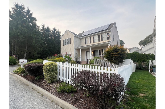 View of front facade featuring a porch, roof mounted solar panels, and a fenced front yard