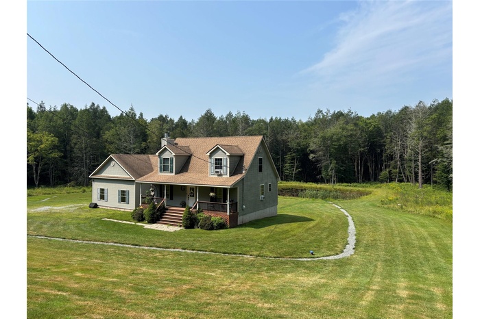 Cape cod home featuring a porch, a front yard, and a view of trees