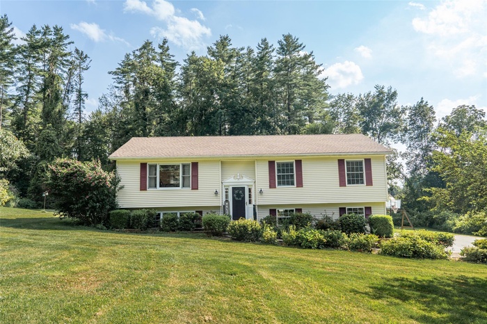 Bi-level home featuring a front lawn and view of wooded area