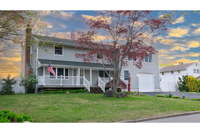 Traditional-style home featuring covered porch, a chimney, an attached garage, driveway, and a front yard