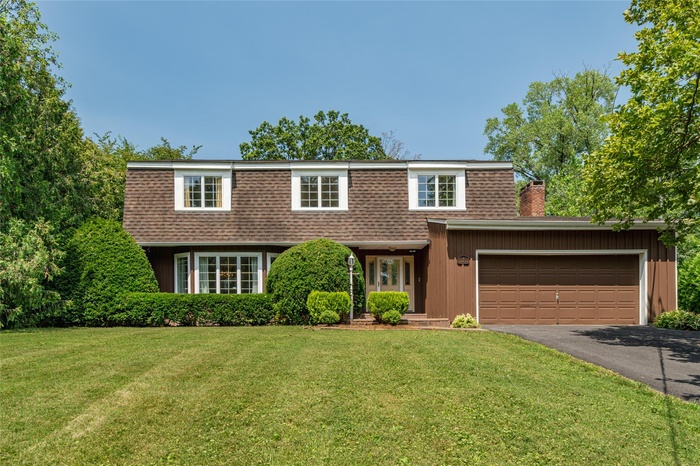 View of front of house featuring driveway, a front lawn, a shingled roof, and a chimney