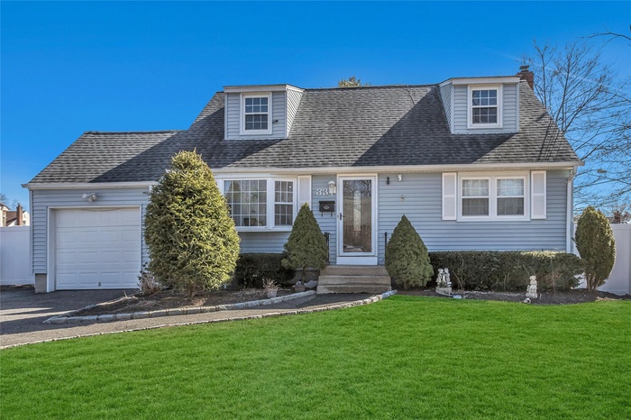 View of front of property with a front lawn, an attached garage, and roof with shingles
