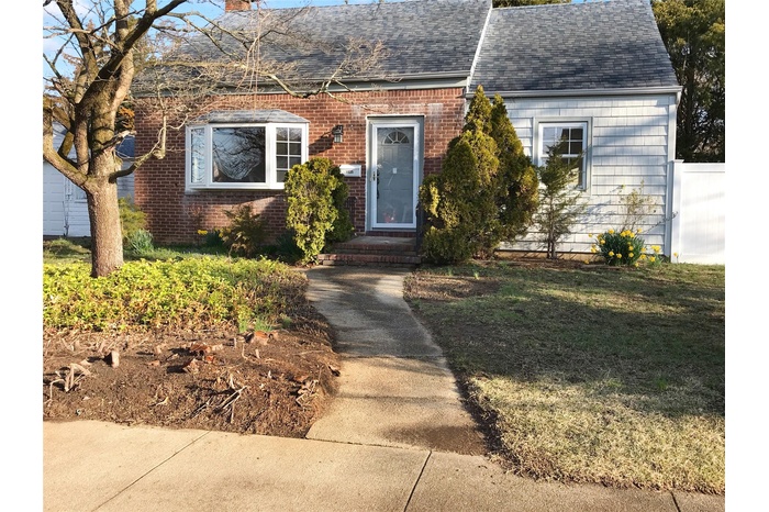 View of front facade featuring brick siding, a chimney, and a shingled roof