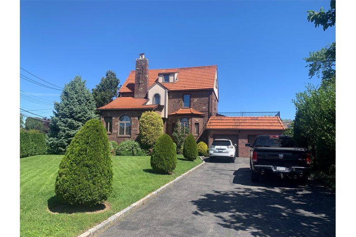 View of front of house with driveway, a chimney, a garage, a tile roof, and a front lawn