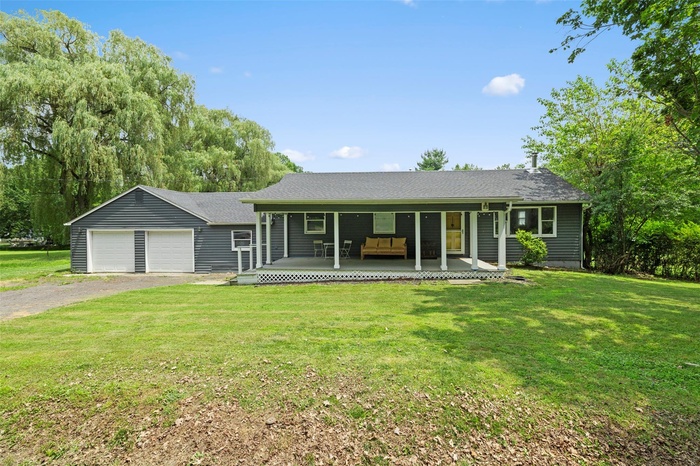 Ranch-style home featuring a porch, a front yard, a garage, driveway, and a shingled roof