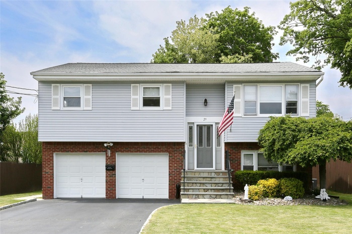 Raised ranch featuring a garage, driveway, entry steps, brick siding, and a front yard