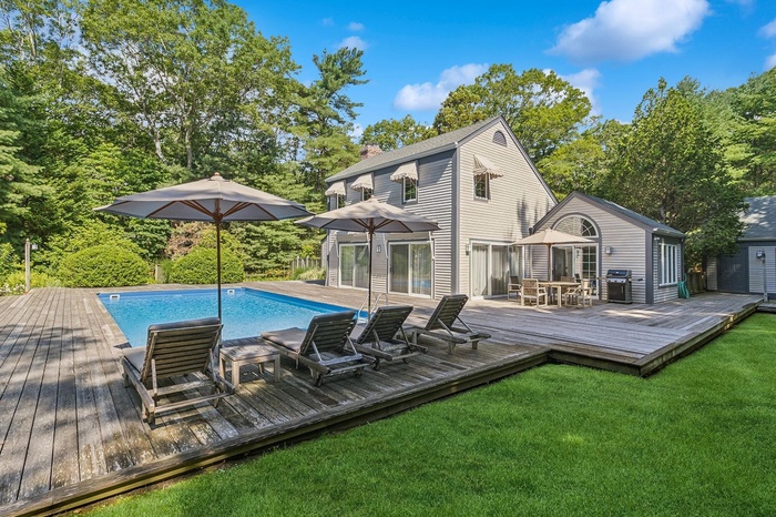 Outdoor pool with a wooden deck, a lawn, a grill, and view of wooded area
