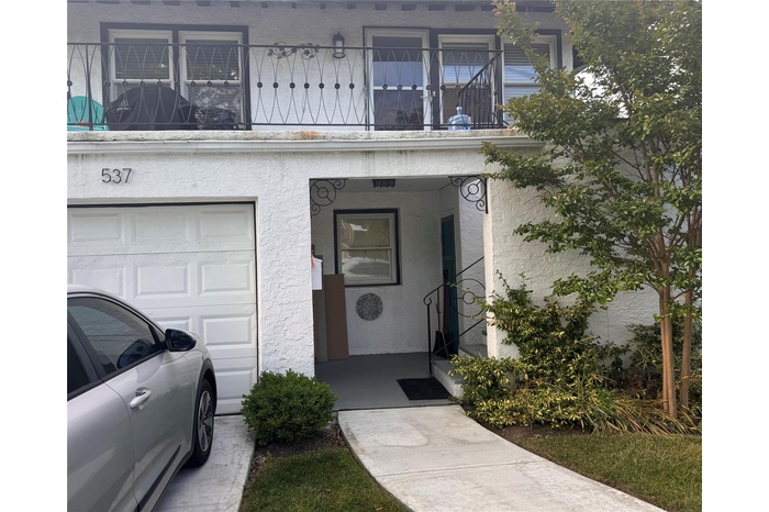 View of exterior entry featuring a garage, stucco siding, a balcony, and covered porch