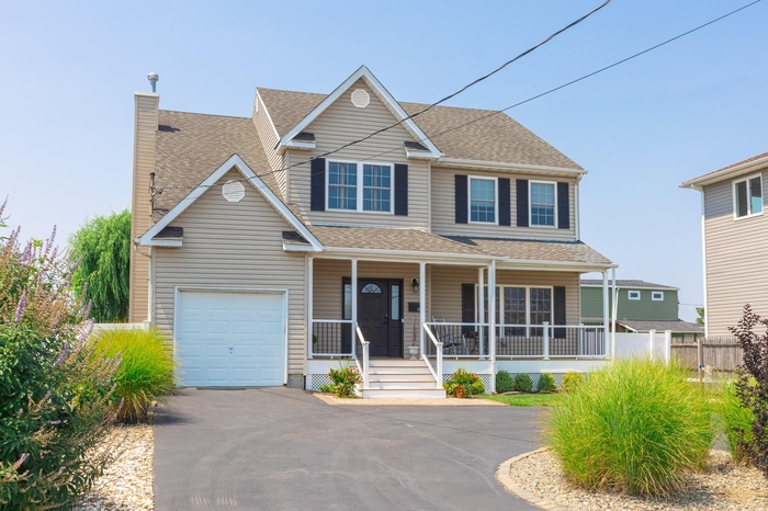 Traditional-style house featuring a shingled roof, covered porch, a chimney, and driveway