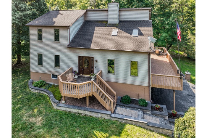 View of front facade with roof with shingles, a wooden deck, a chimney, and a front yard