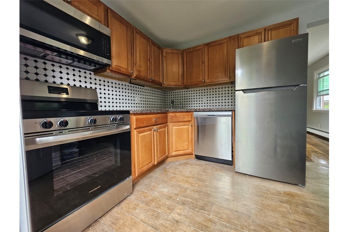 Kitchen with appliances with stainless steel finishes, decorative backsplash, brown cabinets, and dark countertops