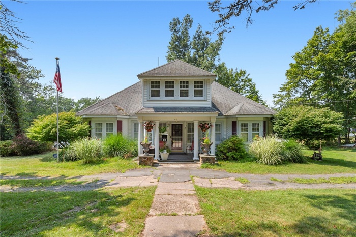View of front of home with a porch, a shingled roof, and a front yard