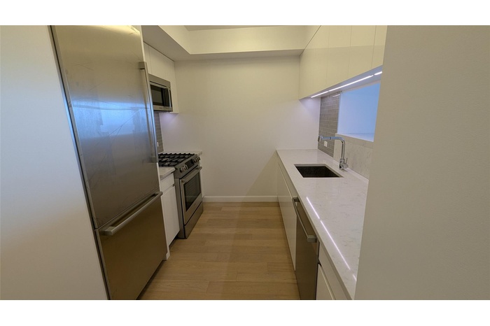Kitchen with white cabinetry, stainless steel appliances, light wood-type flooring, and light countertops