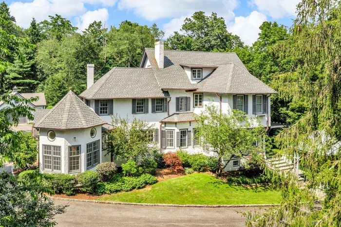 View of front of house featuring a chimney, stucco siding, a front yard, roof with shingles, and view of scattered trees