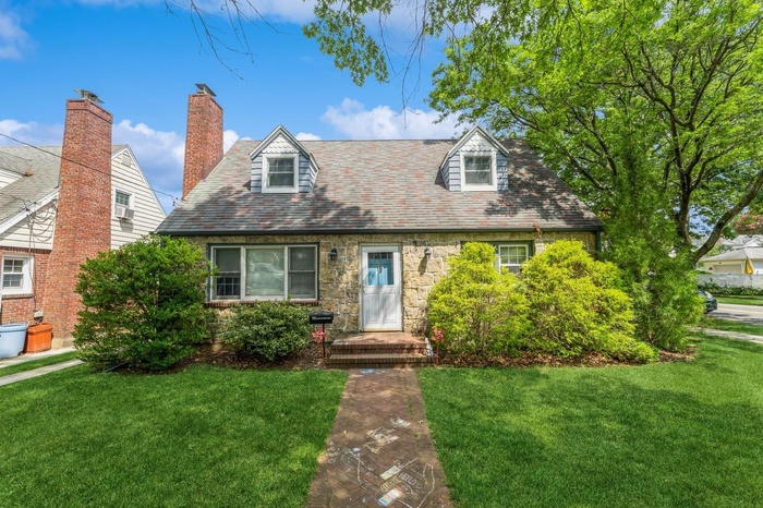 New england style home with a high end roof, a front yard, and stone siding
