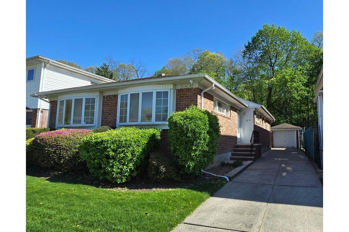 226-18 77 Ave, Oakland Gardens, NY 11364 View of front of property with driveway, a detached garage, brick siding, and an outbuilding