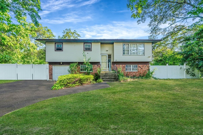Raised ranch featuring brick siding, an attached garage, driveway, and a gate