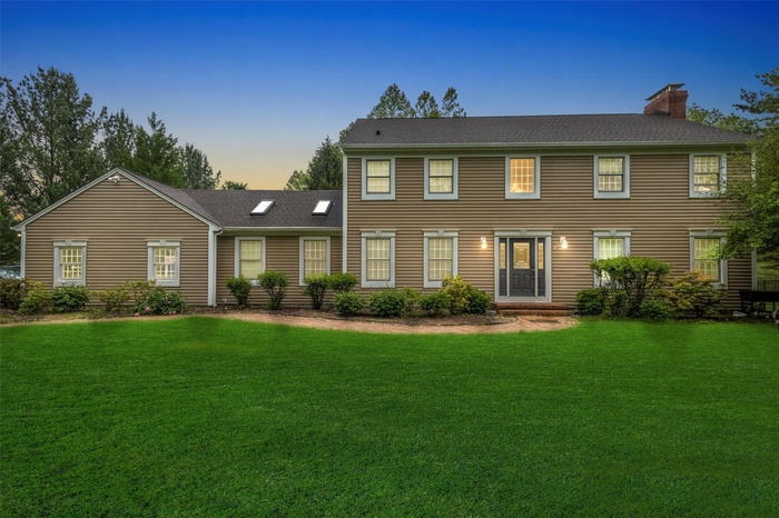 Colonial inspired home with a chimney, a front lawn, and a shingled roof
