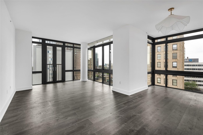 Spacious living room area with floor to ceiling windows, wood finished floors, and french doors