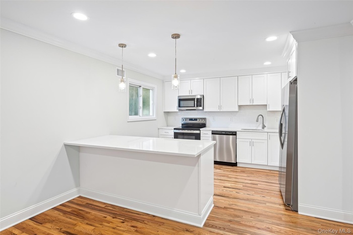 Kitchen featuring ornamental molding, appliances with stainless steel finishes, a peninsula, light wood-type flooring, and white cabinets